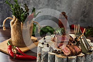 Juicy medium pieces of rib eye beef steak in a pan on a wooden board with a fork and knife
