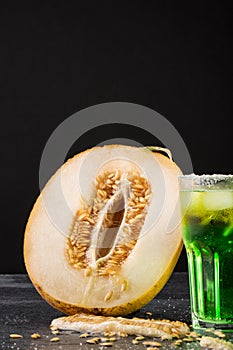 A juicy melon cut in half and cold alcoholic cocktail on a black background. Tasty melon and fresh green cocktail with lime. Sweet