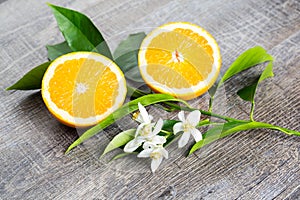 Juicy Orange cut in two parts and neroli, flowers of orange tree, on rustic wood background.