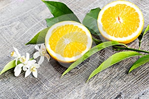 Juicy Orange cut in two parts and neroli, flowers of orange tree, on rustic wood background.