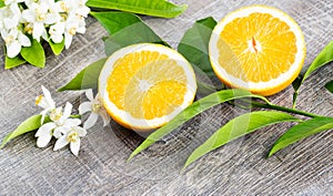 Juicy Orange cut in two parts and neroli, flowers of orange tree, on rustic wood background.