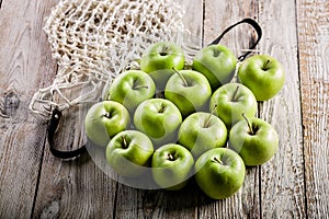 Juicy organic green apples and cotton string mesh bag on a wooden table