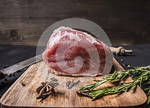 Juicy piece of fresh raw pork steak on vintage cutting board with herbs and spices wooden rustic background close up