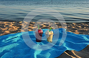 Pieces of fruit in glasses on a blue blanket on the sandy beach. watermelon and melon at sunset. background for the design.