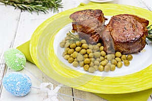 Juicy pork medallions wrapped in bacon, serve with green peas and a sprig of rosemary on a plate on white wooden background.