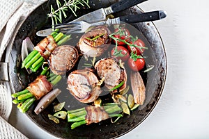 Juicy pork medallions wrapped in bacon, serve on the iron pan on the dark wooden dackground. Close up.