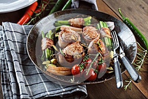 Juicy pork medallions wrapped in bacon, serve on the iron pan on the dark wooden dackground. Close up.