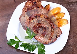 Juicy pork neck chops are grilled with potatoes on a white plate.