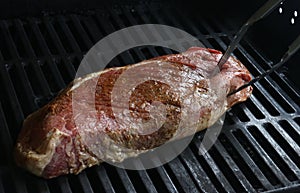 Juicy raw London Broil on grill with thongs