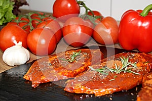 Juicy raw meat marinated with spices on a black board, steaks with rosemary, red tomatoes, paprika, garlic, dill, concept of