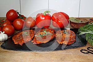 Juicy raw meat marinated with spices on a black board, steaks with rosemary, red tomatoes, paprika, garlic, dill, concept of