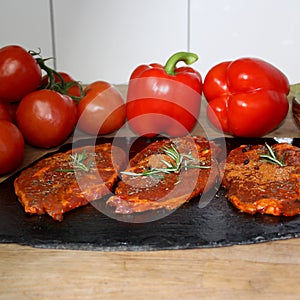 Juicy raw meat marinated with spices on a black board, steaks with rosemary, red tomatoes, paprika, garlic, dill, concept of