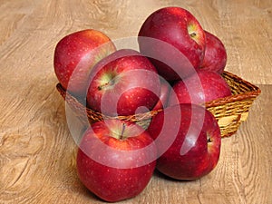 Juicy red organic apples in a basket on oak tree wood background. Autumn Fall season orchard harvest production.