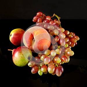 Juicy red ripe pears, plums, peach and grapes fruits on black background
