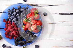 Juicy ripe organic berries of strawberries, blueberries, blackberries, raspberries on a blue plate on a light wooden background.