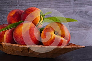 Juicy and ripe peaches lie in a carved wooden plate