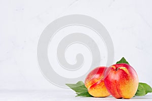 Juicy ripe whole nectarines peaches with young green leaves in soft light white wood board.