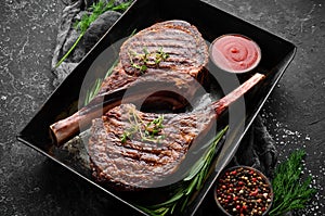 Juicy steak grilled on the bone with spices and herbs. On a black stone background. Top view. Free copy space