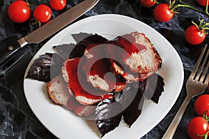 Juicy steak well done roast pork with red sauce and Basil leaves on a white plate over a black marble table