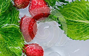 juicy strawberry berries and green mint leaves in ice water close-up top view
