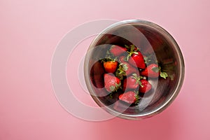 Juicy strawberry in metal bowl on pink background. View from the top.