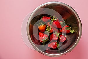 Juicy strawberry in metal bowl on pink background. View from the top.