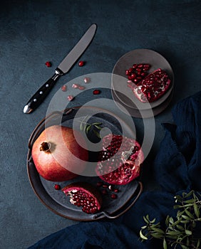 A juicy sweet red pomegranate lies broken on an antique plate on a dark background