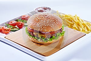 Juicy tasty hamburger on a wooden cutting board with french fried fries, vegetables and ketchup. Isolated composition on