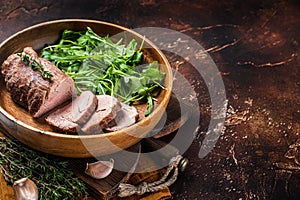 Juicy tenderloin Steak, sliced Roast beef in wooden plate with arugula. Dark background. Top view. Copy space