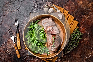 Juicy tenderloin Steak, sliced Roast beef in wooden plate with arugula. Dark background. Top view. Copy space