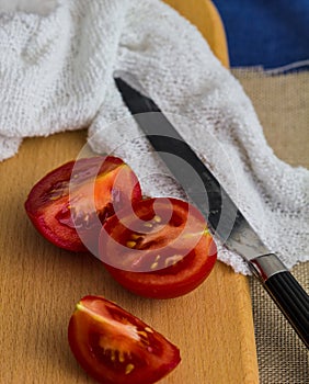 Juicy tomato pieces with knife against a wood board background and textiles with copy space