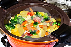 Juicy Vegetable stew, on the stove in an orange ceramic pot. Vegetarianism.