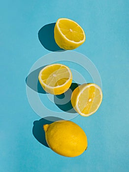 Juicy whole and half lemon and slices on bright pastel blue background. Minimal top view summer concept