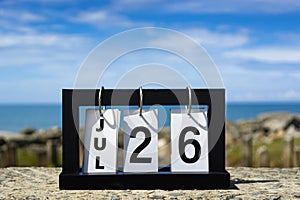 Jul 26 calendar date text on wooden frame with blurred background of ocean.