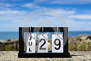 Jul 29 calendar date text on wooden frame with blurred background of ocean.