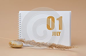 july 01. 01th day of the month, calendar date.White blank sheet of notepad, stones, dry sprig of grass, on beige