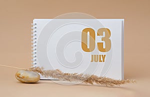 july 03. 03th day of the month, calendar date.White blank sheet of notepad, stones, dry sprig of grass, on beige