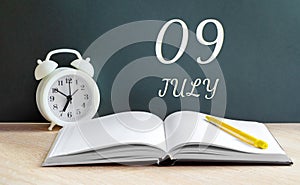 july 09. 09-th day of the month, calendar date.A white alarm clock, an open notebook with blank pages, and a yellow