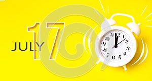 July 17th. Day 17 of month, Calendar date. White alarm clock with calendar day on yellow background. Minimalistic concept of time