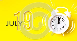 July 19th. Day 19 of month, Calendar date. White alarm clock with calendar day on yellow background. Minimalistic concept of time