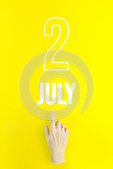 July 2nd. Day 2 of month, Calendar date.Hand finger pointing at a calendar date on yellow background.Summer month, day of the year