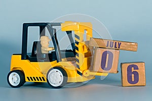 july 6th. Day 6 of month, Construction or warehouse calendar. Yellow toy forklift load wood cubes with date. Work planning and