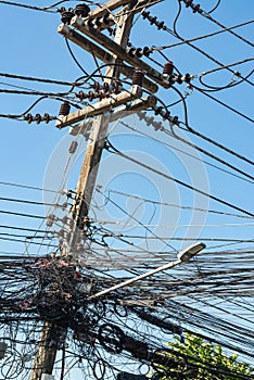 A jumble of electrical and telephone wires attached to a utility pole in Thailand