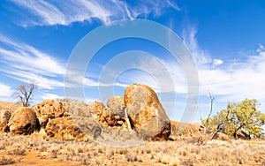 A jumble of granite boulders, blue sky with strange clouds and dry grass landscape