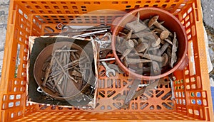 Jumble of old rusty nails and hand tools in a orange plastic box.