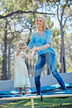 Jump around. a young mother playing on the trampoline with her daughter outside.