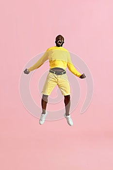 Jump. Black man jumping in air and screaming on pink background
