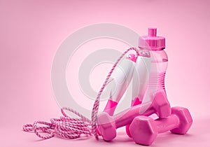 Jump rope, bottle of water and dumbbells on pink background