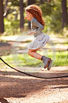 Jump, rope and girl outdoor for game in forest, park or playing on summer, holiday and vacation. Child, skipping and