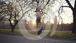 Jump rope workout of a young Caucasian girl in the autumn park on sunset. Woman in black sportwear training outdoors